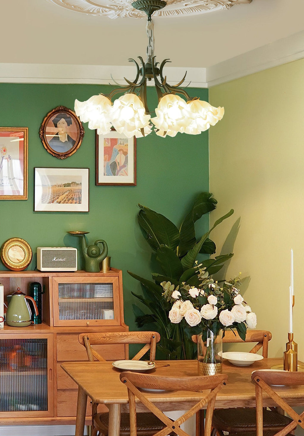 In a green dining room hung with portraits, this Clérachic chandelier glows above a wooden table.