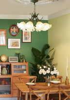 In a green dining room hung with portraits, this Clérachic chandelier glows above a wooden table.