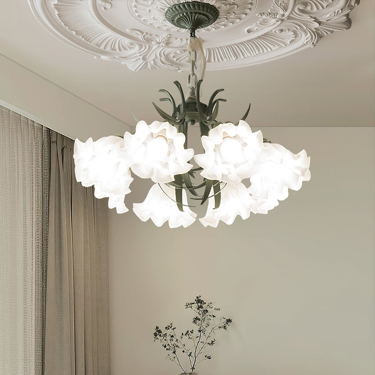 Beside sage-green curtains, this Clérachic chandelier hangs lit at an angle, its shades glowing warm.