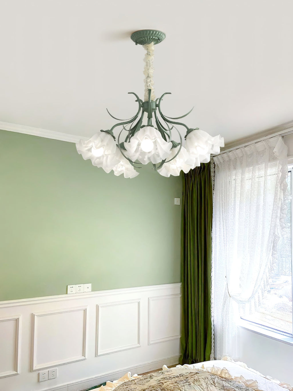 In a green wainscoted bedroom, this Clérachic chandelier lights the space beside a curtained window.