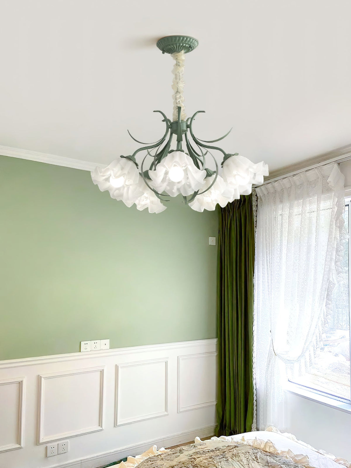 In a green wainscoted bedroom, this Clérachic chandelier lights the space beside a curtained window.