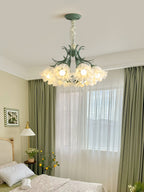 In a bedroom with sage-green curtains, this Clérachic chandelier glows warm above the bed.
