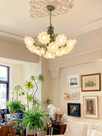Amid potted plants and a gallery wall, this Clérachic chandelier glows warm in a bright living room.