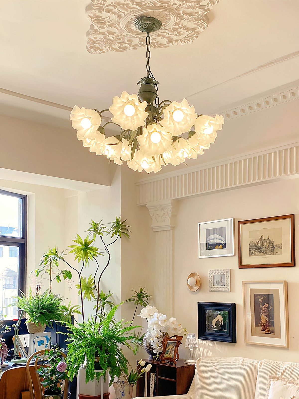 Amid potted plants and a gallery wall, this Clérachic chandelier glows warm in a bright living room.
