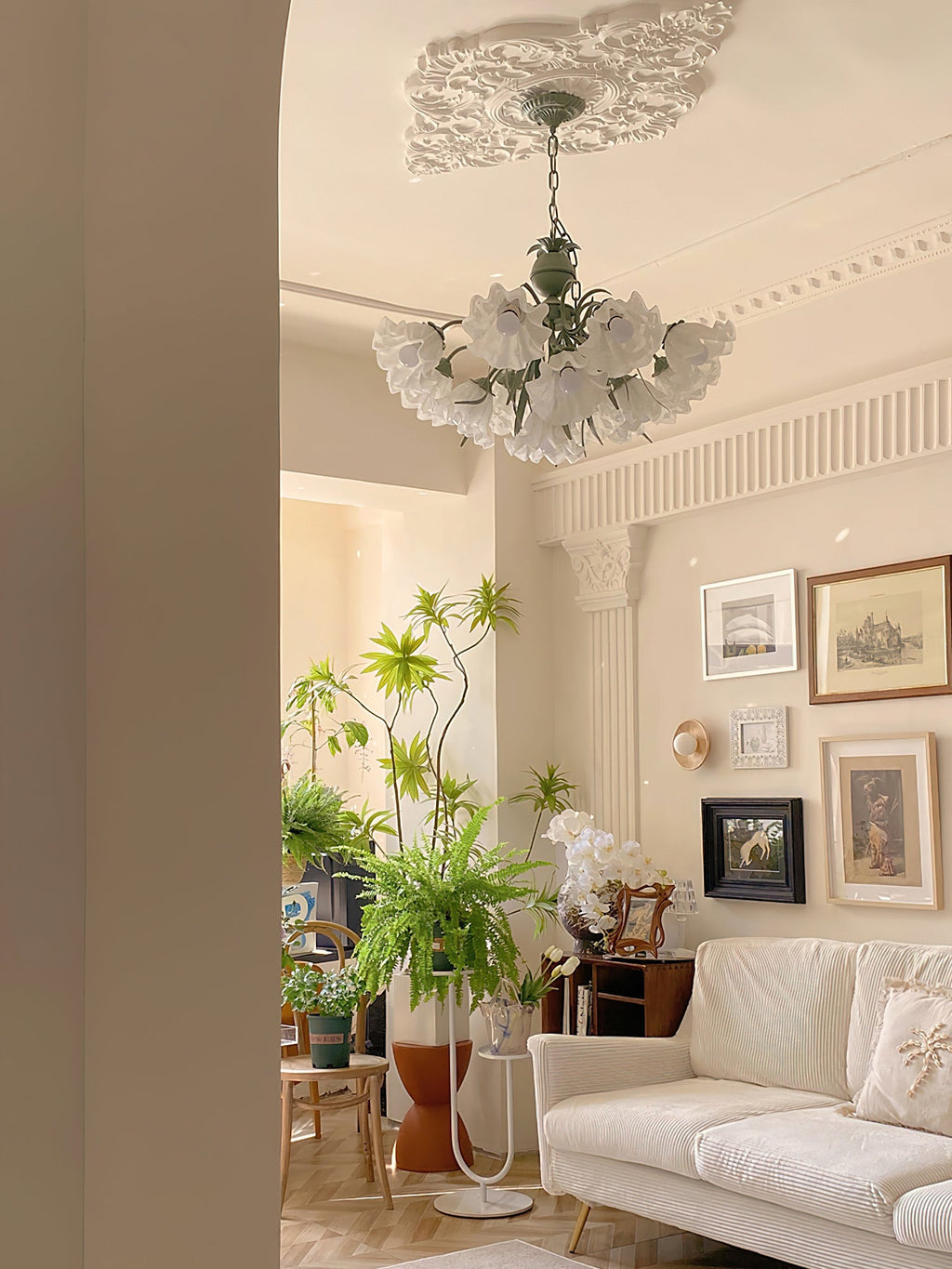Between fluted columns in a plant-filled living room, this Clérachic chandelier lights the space.