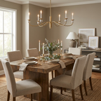 In a dining room corner with tall windows, this Clérachic chandelier in brushed brass lights a wood table beneath a console lamp and framed art.