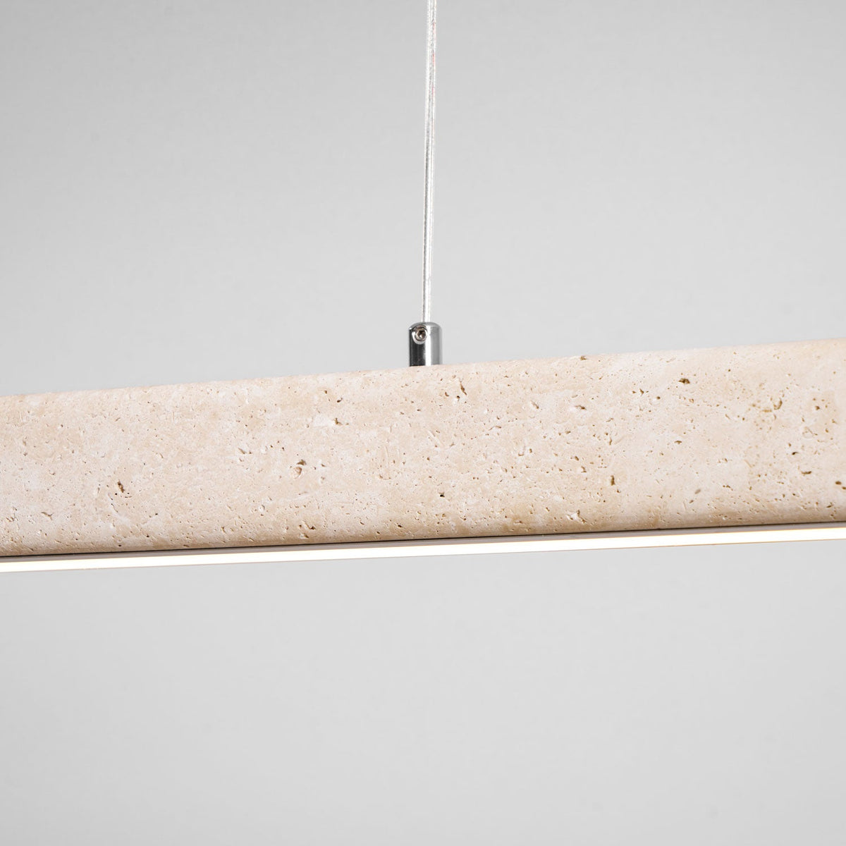 Close view of the travertine's natural pitting on this Clérachic pendant, its LED strip glowing warm along the underside.