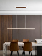 This Clérachic pendant hangs from a pale wood canopy, its travertine bar glowing warm above a marble dining table.