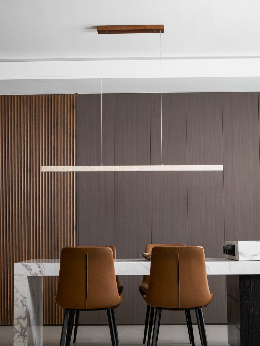 A dark wood canopy holds this Clérachic pendant's travertine bar, glowing warm above a marble dining table.