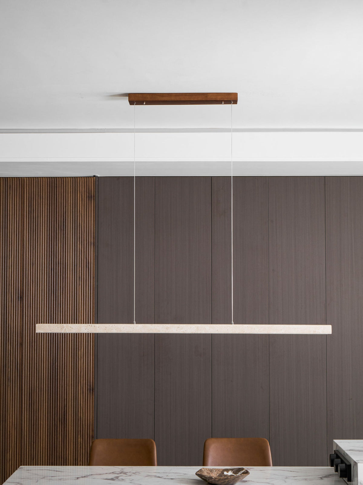 A wider view of the dining room shows this Clérachic pendant's travertine bar glowing warm beside open shelving and wine bottles.