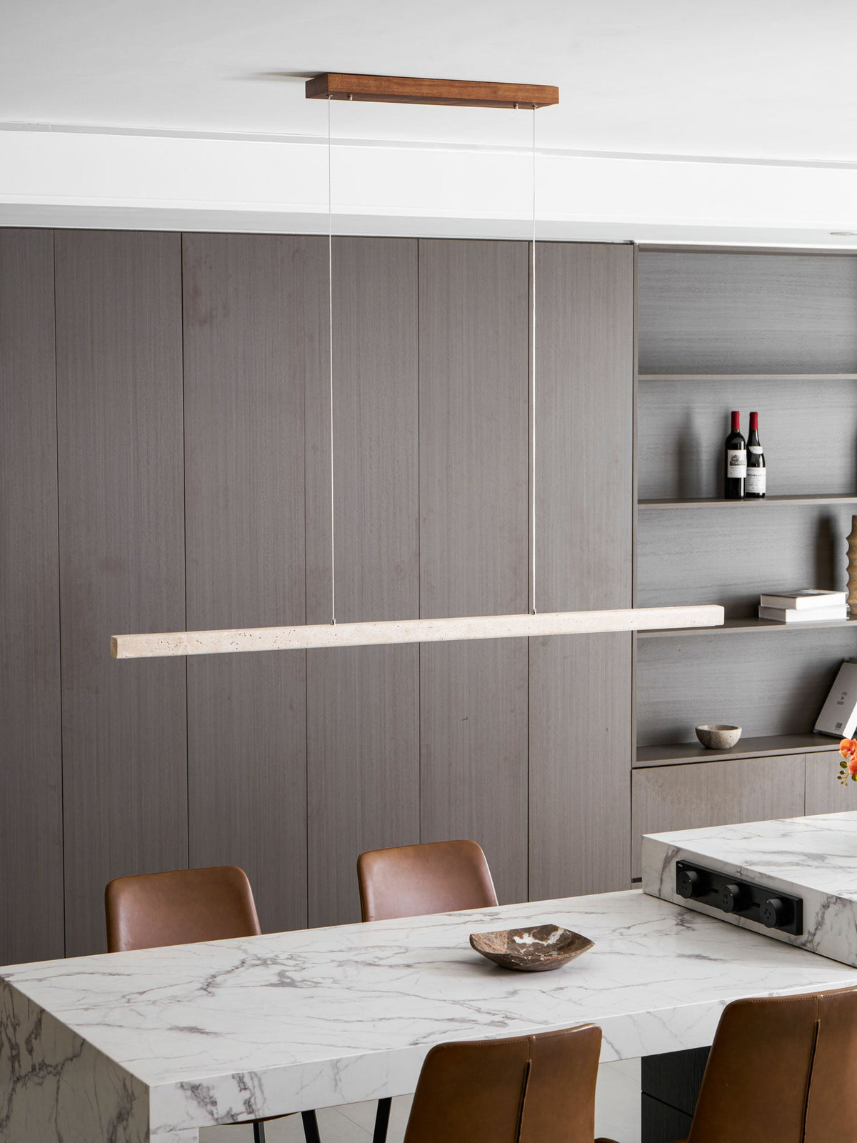 Open shelving with wine bottles sits behind this Clérachic pendant, its travertine bar glowing warm above the marble table.