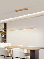This Clérachic pendant hangs its travertine bar above a dining table set with a stoneware jug and trailing greenery, glowing warm along its length.