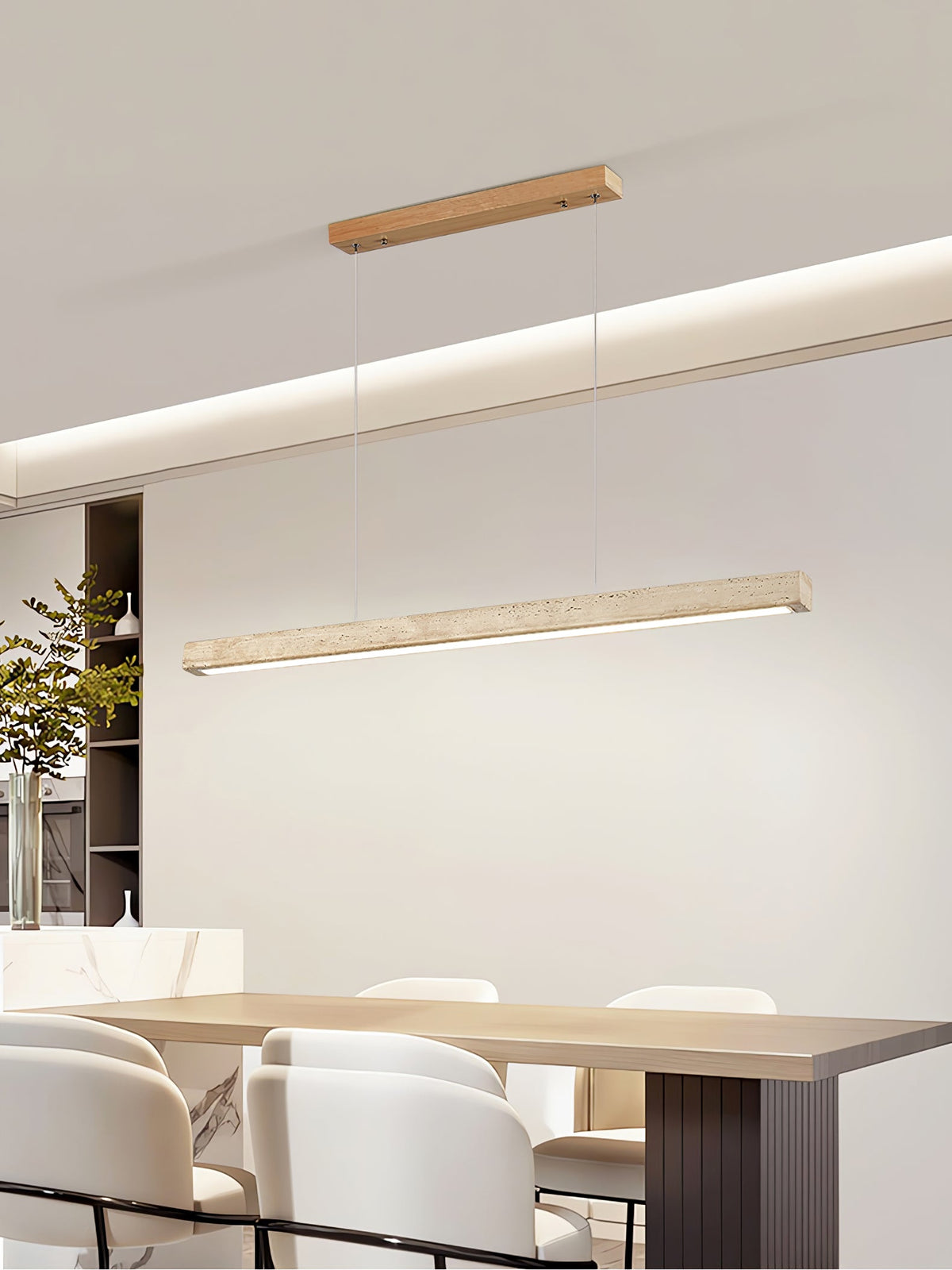 This Clérachic pendant hangs its travertine bar above a dining table set with a stoneware jug and trailing greenery, glowing warm along its length.