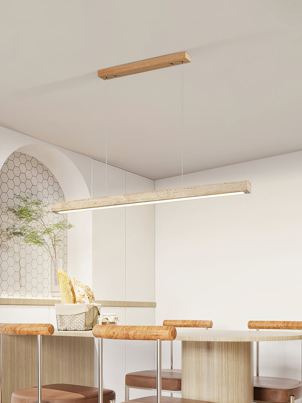 Beside an arched alcove and a potted plant, this Clérachic pendant's travertine bar glows warm above a kitchen table.