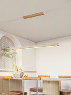 Beside an arched alcove and a potted plant, this Clérachic pendant's travertine bar glows warm above a kitchen table.
