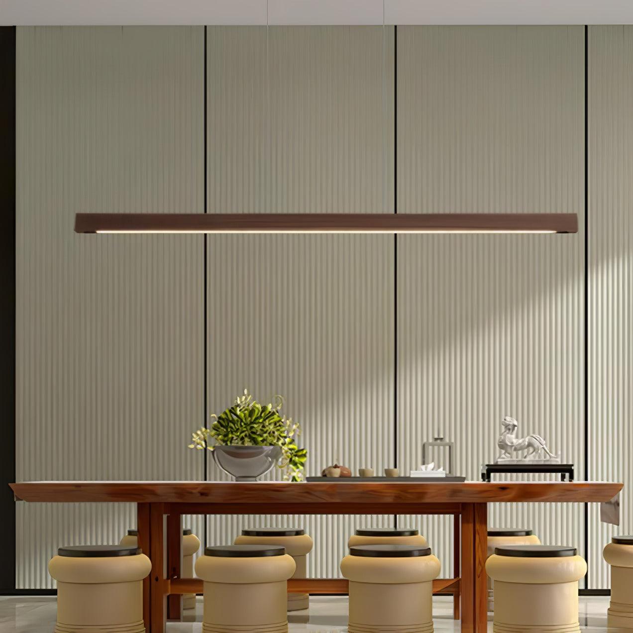Linear wooden pendant light glowing above a desk workspace