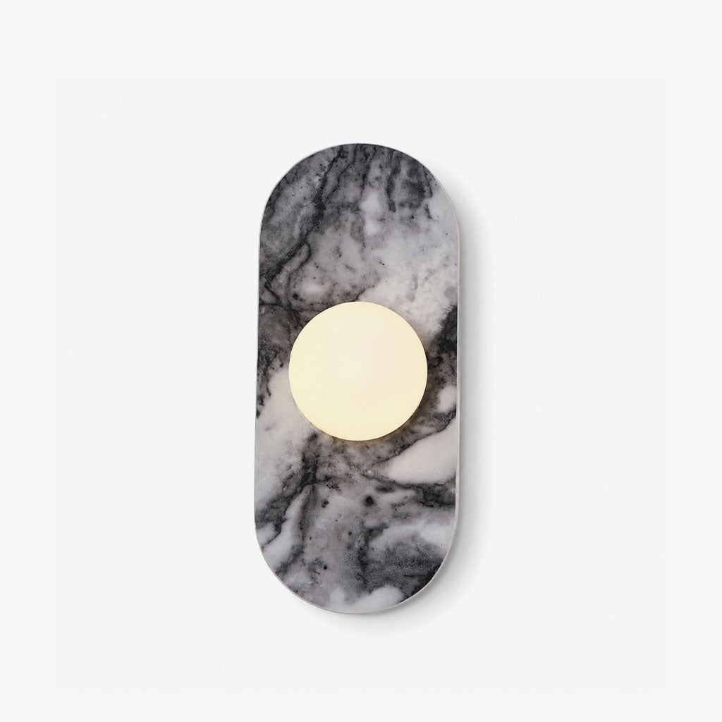 This Clérachic wall sconce shows a capsule-shaped natural stone plaque with a single warm glass orb centred on its veined grey surface, on a plain backdrop.