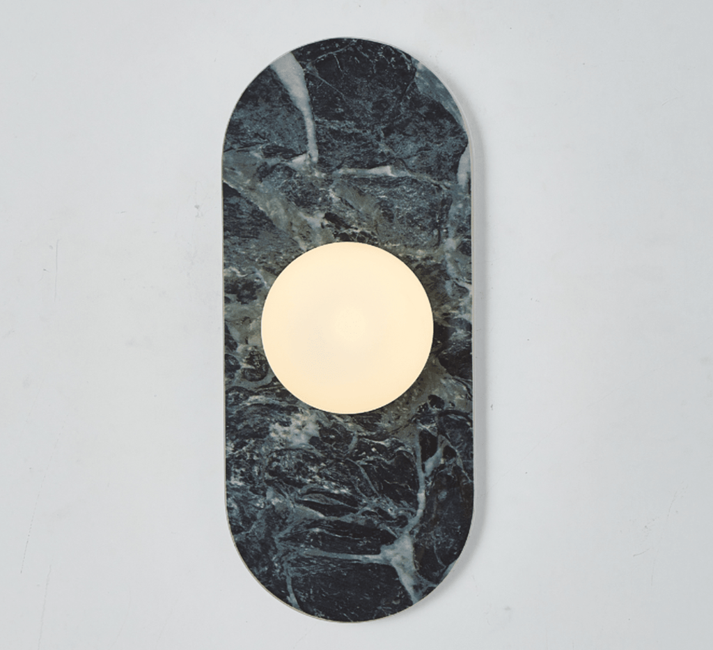 A deep green marble Clérachic wall sconce hangs isolated on a plain wall, its glass globe glowing at the centre.