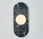 A deep green marble Clérachic wall sconce hangs isolated on a plain wall, its glass globe glowing at the centre.