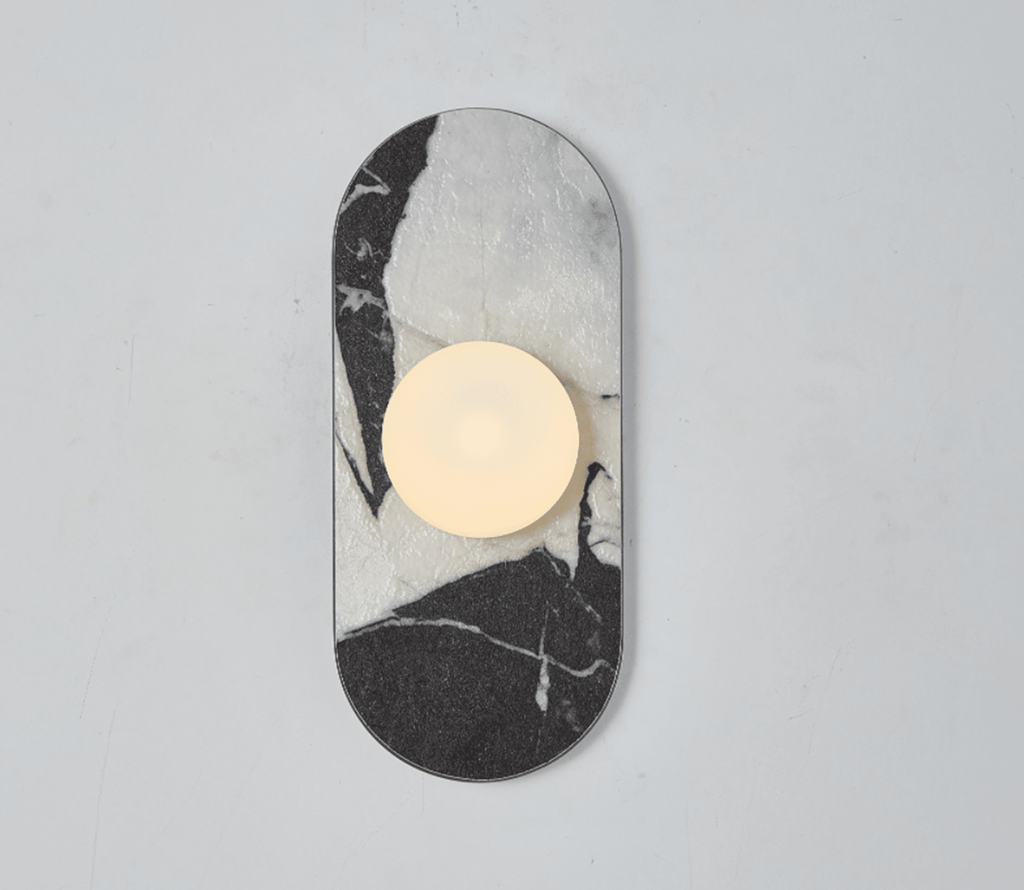 A black-and-white marble Clérachic wall sconce hangs isolated on a plain wall, its glass globe glowing above the veining.