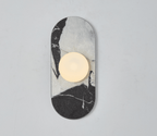 A black-and-white marble Clérachic wall sconce hangs isolated on a plain wall, its glass globe glowing above the veining.