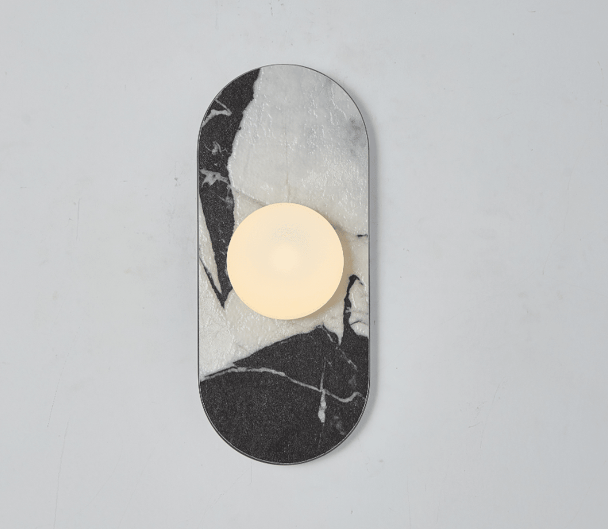 A black-and-white marble Clérachic wall sconce hangs isolated on a plain wall, its glass globe glowing above the veining.