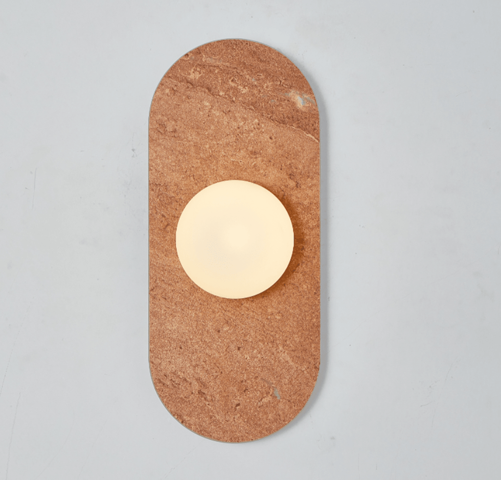 A red travertine Clérachic wall sconce glows alone against a plain wall, its warm stone tone catching the light.
