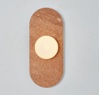 A red travertine Clérachic wall sconce glows alone against a plain wall, its warm stone tone catching the light.