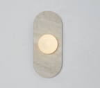 A beige travertine Clérachic wall sconce glows alone on a plain wall, its round glass globe lit warm at its centre.