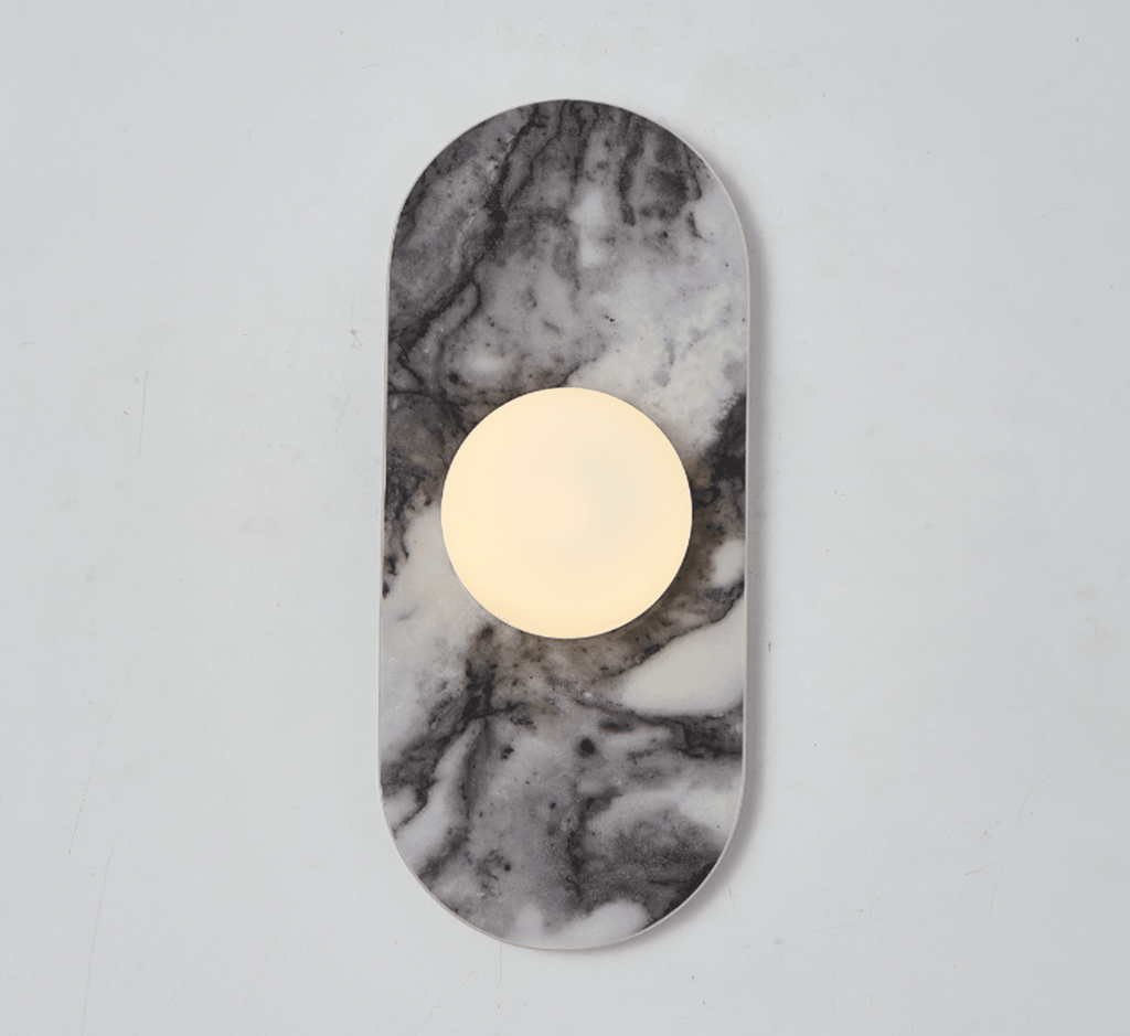 A pale grey marble Clérachic wall sconce hangs isolated against a plain wall, its glass globe glowing softly at its centre.