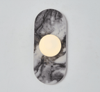 A pale grey marble Clérachic wall sconce hangs isolated against a plain wall, its glass globe glowing softly at its centre.