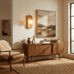 The Clérachic wall sconce glows above a wooden sideboard beside a framed abstract print and a leather armchair.