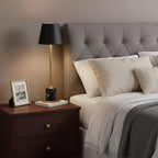 A Clérachic marble table lamp lights a nightstand beside a grey tufted headboard, a small framed photo propped next to it.