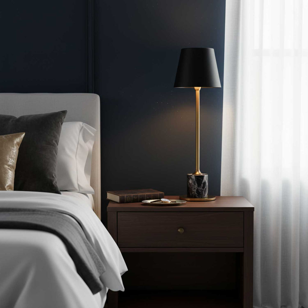 A Clérachic marble table lamp glows on a nightstand against a navy wall, sheer curtains lit by the window behind it.