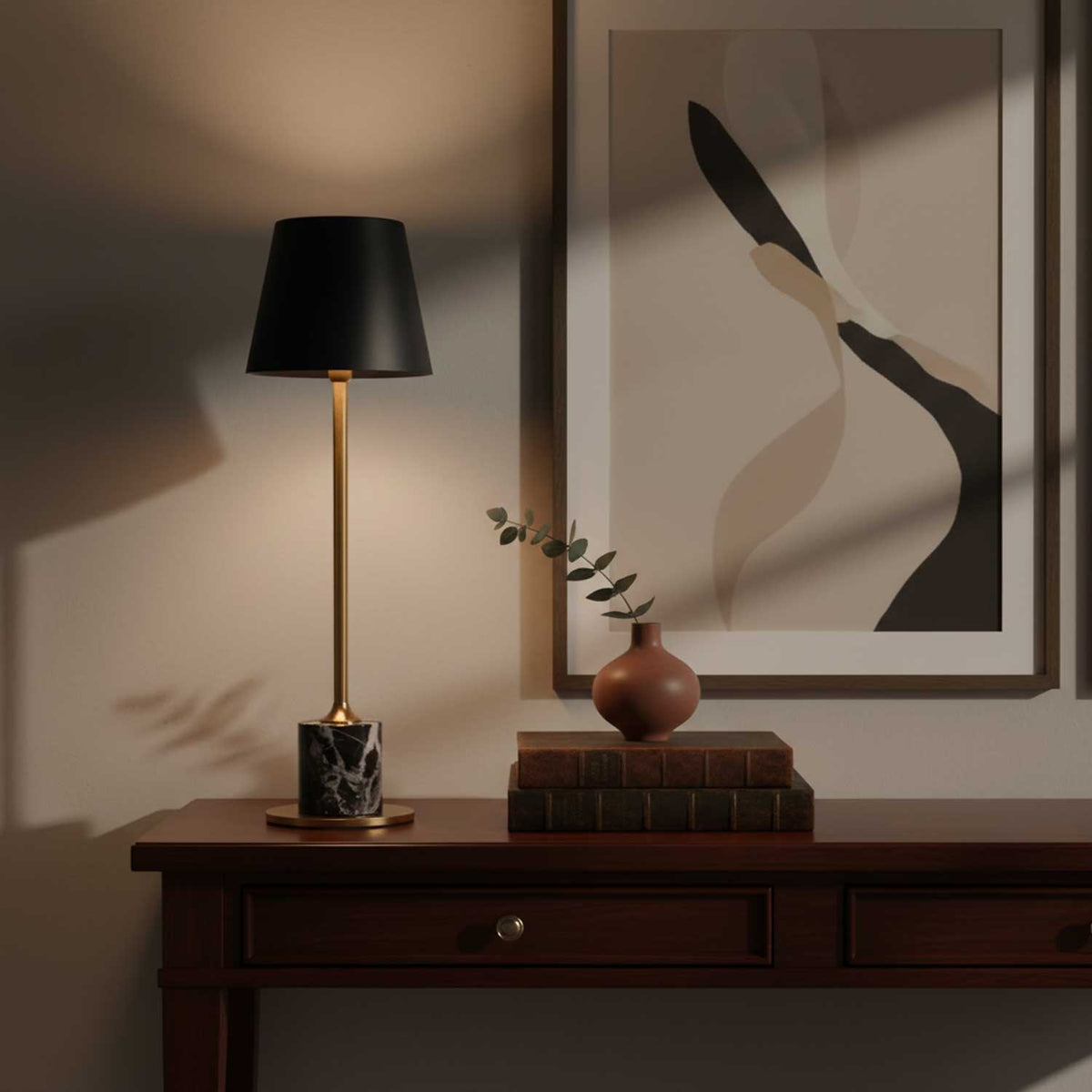 A Clérachic marble table lamp stands on a wooden console table below an abstract print, a terracotta vase and books beside it.