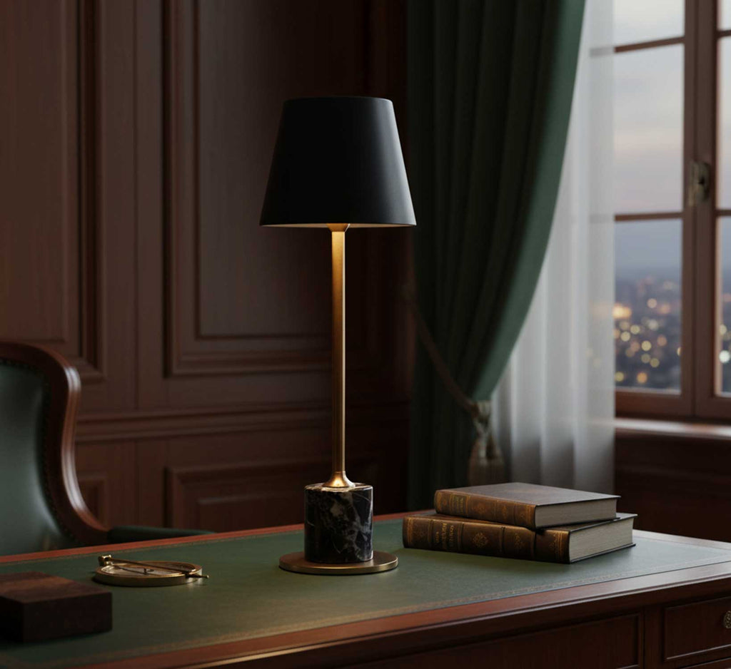 A Clérachic marble table lamp lights a green leather desktop near a window, books and glasses laid out in a dusk-lit study.
