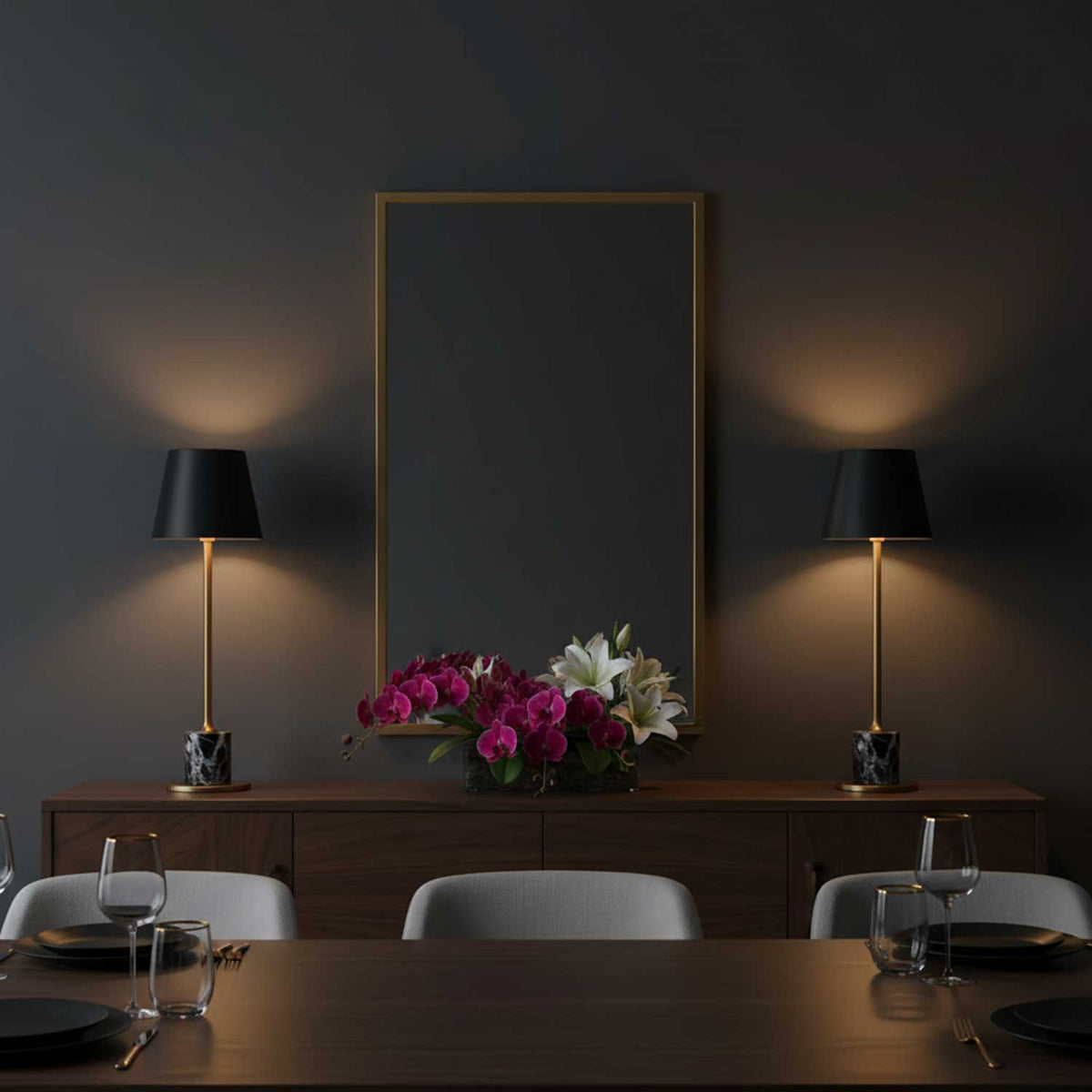 Two Clérachic marble table lamps flank a gilt mirror on a dark sideboard, with roses and lilies set between them in a dining room.