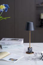 A Clérachic marble table lamp on a marble tabletop with magazines and a mug, blue flower stems visible in the upper corner.