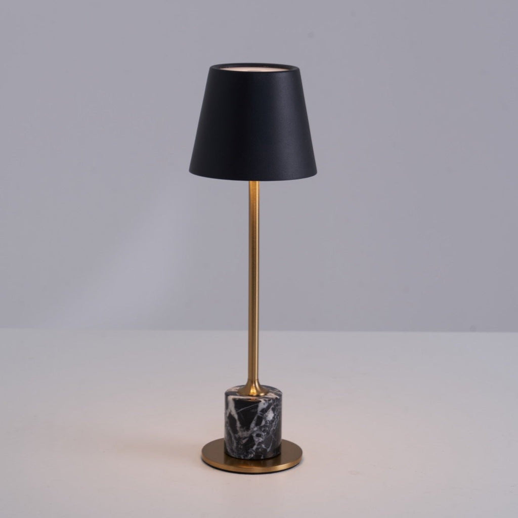 Angled slightly against a medium grey backdrop, this Clérachic table lamp pairs its brass stem with a black tapered shade and a dark marble base.
