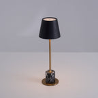 Lit warm on a plain tabletop, the black shade of this Clérachic lamp glows above its slim brass stem and dark marble cylinder base.