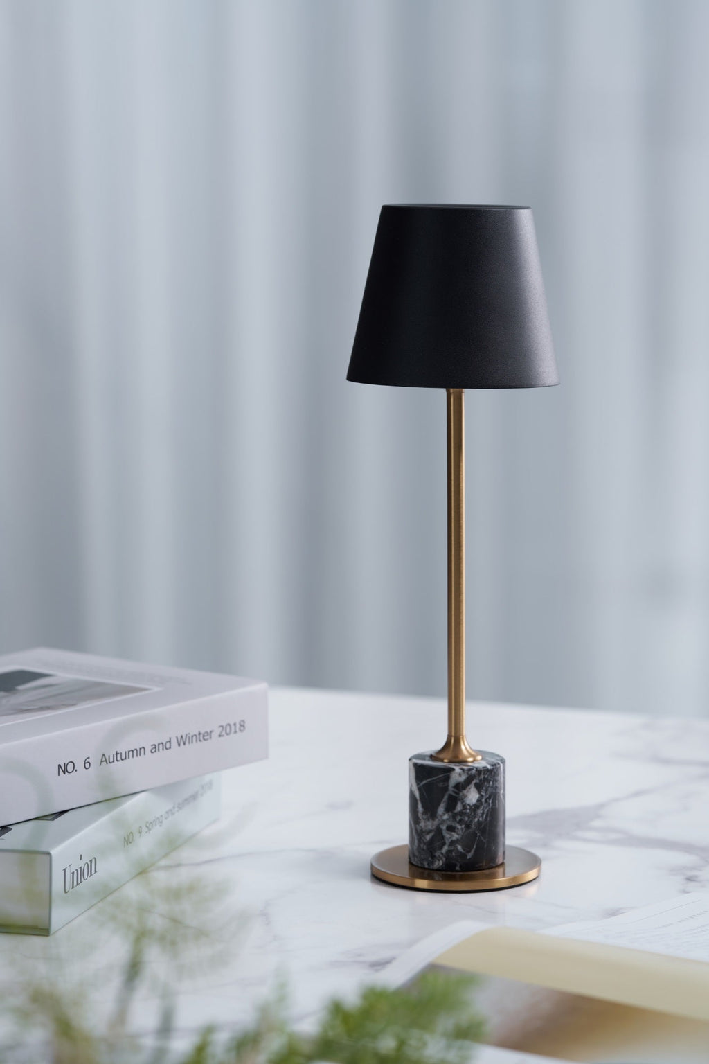 Beside a small stack of books and a sprig of greenery, this Clérachic table lamp's brass stem and black shade rest on a marble-topped surface.