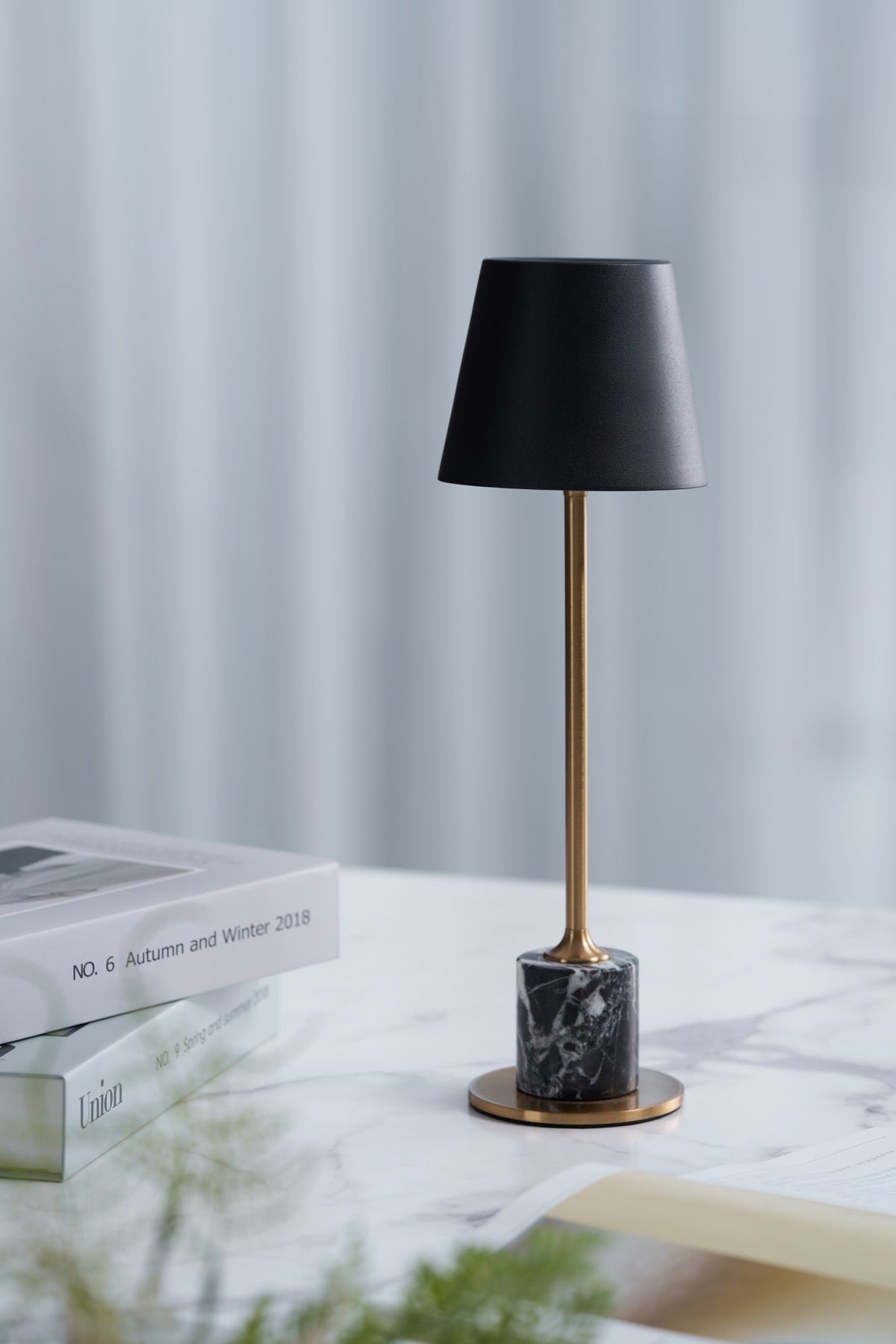Beside a small stack of books and a sprig of greenery, this Clérachic table lamp's brass stem and black shade rest on a marble-topped surface.