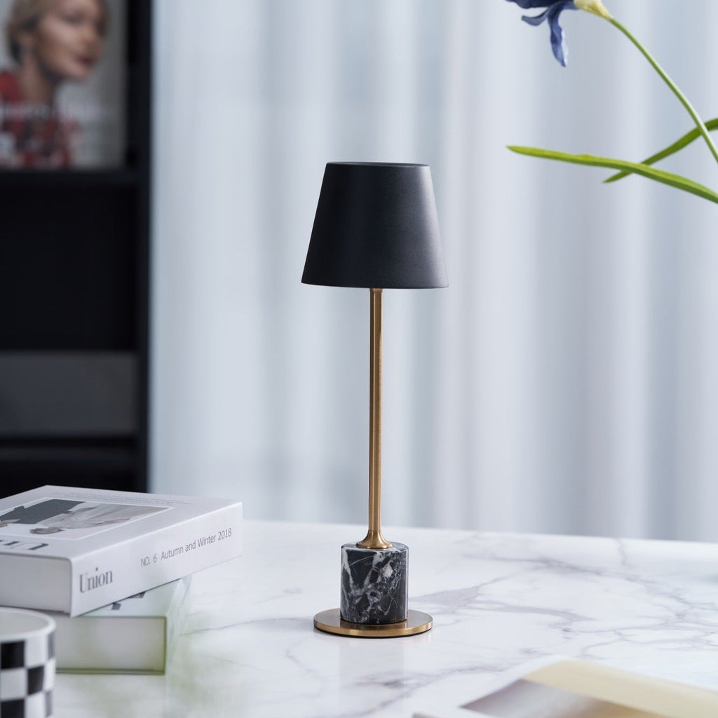 A Clérachic marble table lamp stands on a marble surface near a sheer curtain, a stacked magazine box set beside it.