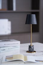 On a marble-topped surface with books stacked nearby, this Clérachic table lamp's brass stem and dark marble base sit against a softly blurred interior.