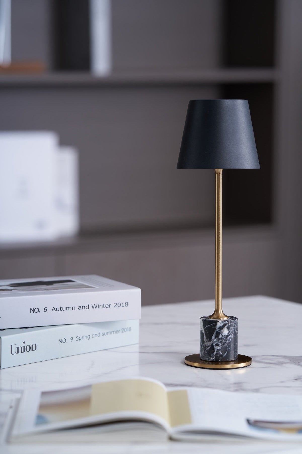 On a marble-topped surface with books stacked nearby, this Clérachic table lamp's brass stem and dark marble base sit against a softly blurred interior.