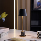A Clérachic black marble table lamp glows on a white marble worktop beside stacked magazines and a chequered mug.