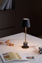 A Clérachic marble table lamp glows on marble with a dried orange branch nearby, candlelight blurred in the background.