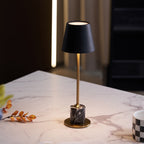 A Clérachic marble table lamp glows on a white marble slab, seen from above with a dried branch and chequered mug nearby.