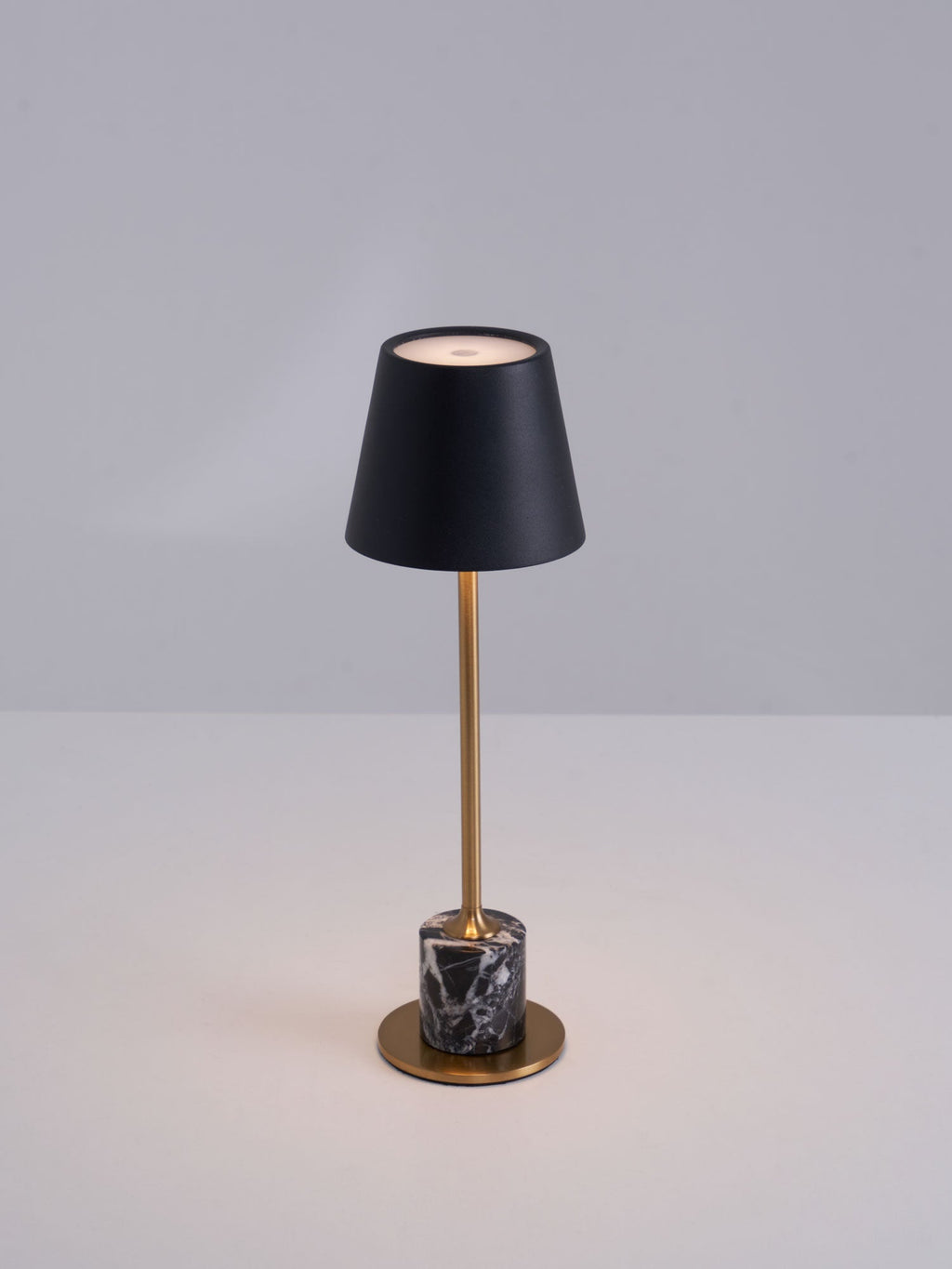 A Clérachic marble table lamp lit against a plain grey backdrop, cropped close to show the full stem and shade.