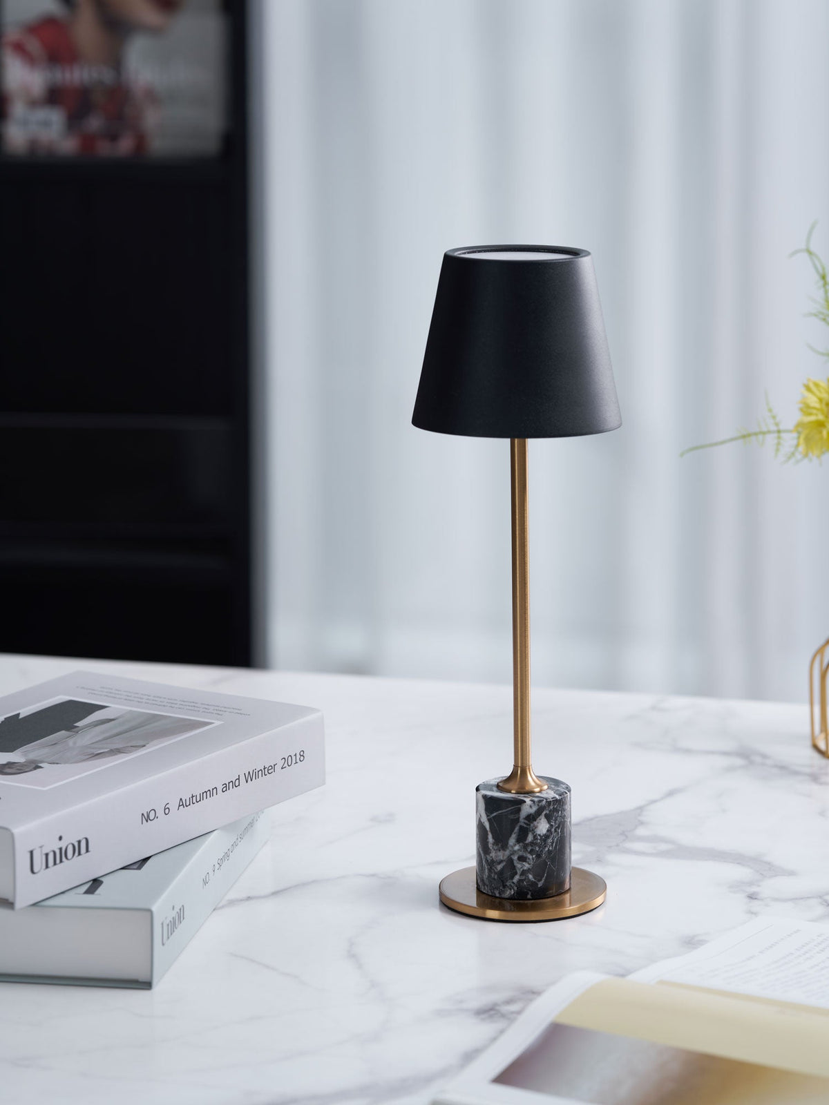 A Clérachic marble table lamp stands on a marble surface beside a sheer curtain, framed straight-on with a magazine box nearby.
